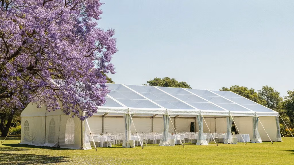 White clear-span frame marquee with round tables beside a jacaranda tree on a Pretoria lawn